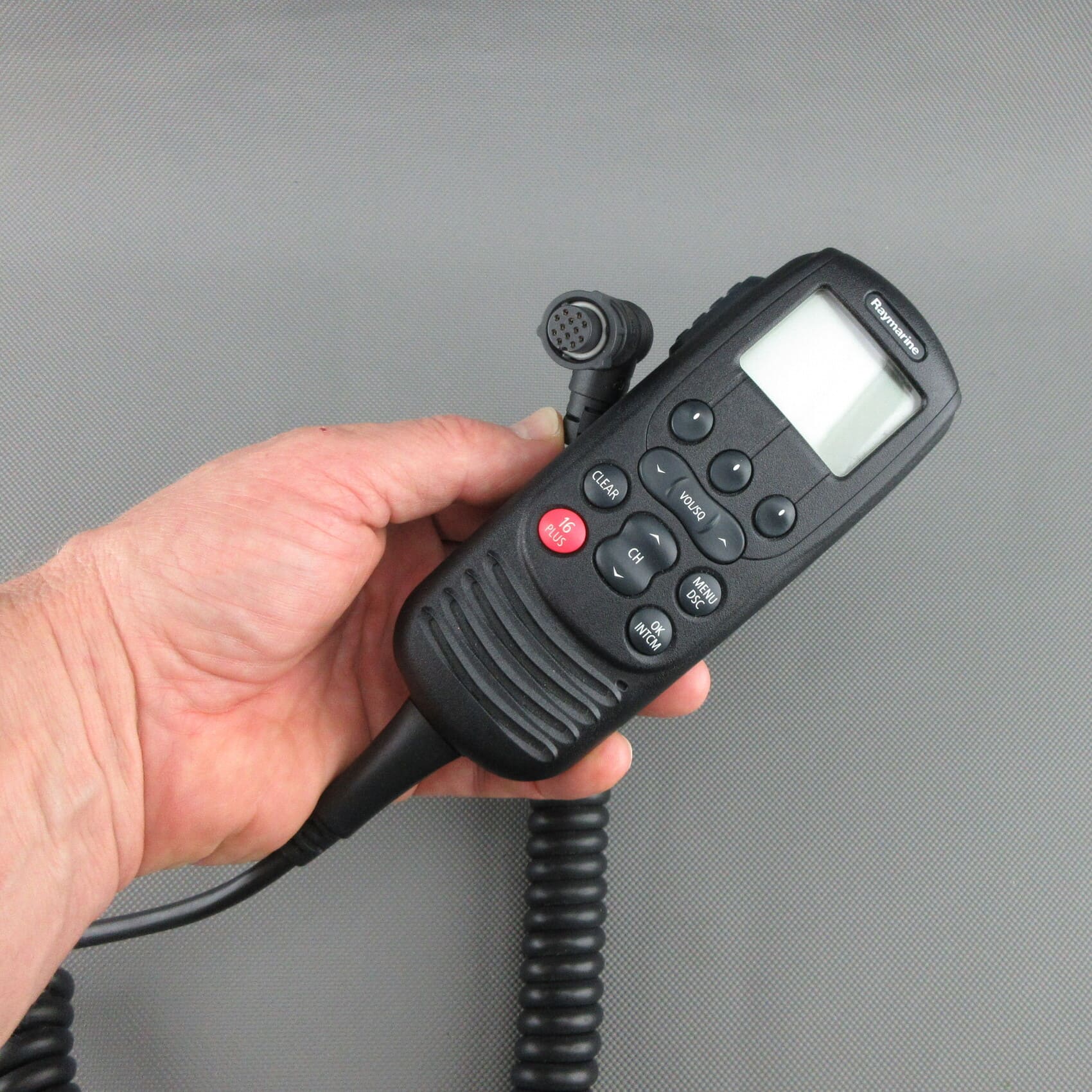 In der Hand gehaltenes, generalüberholtes Raymarine® Ray260 VHF Handset A80197 in Vorderansicht mit Anschlusstecker.