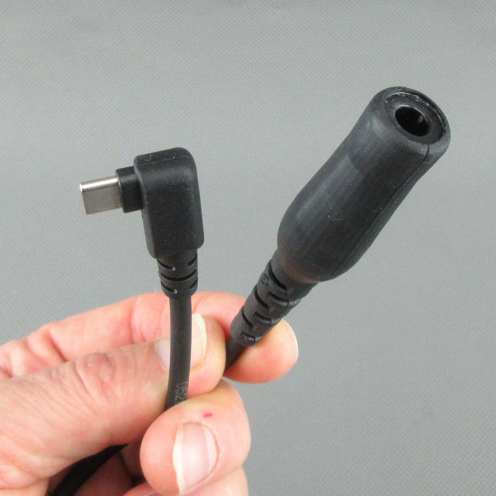 Hand holding the StarCom1 FLX2 adapter cable, focusing on the angled USB-C plug and the TP-120 coupling socket (Nexus® / Amphenol® compatible) for connecting NATO-wired tactical headsets.